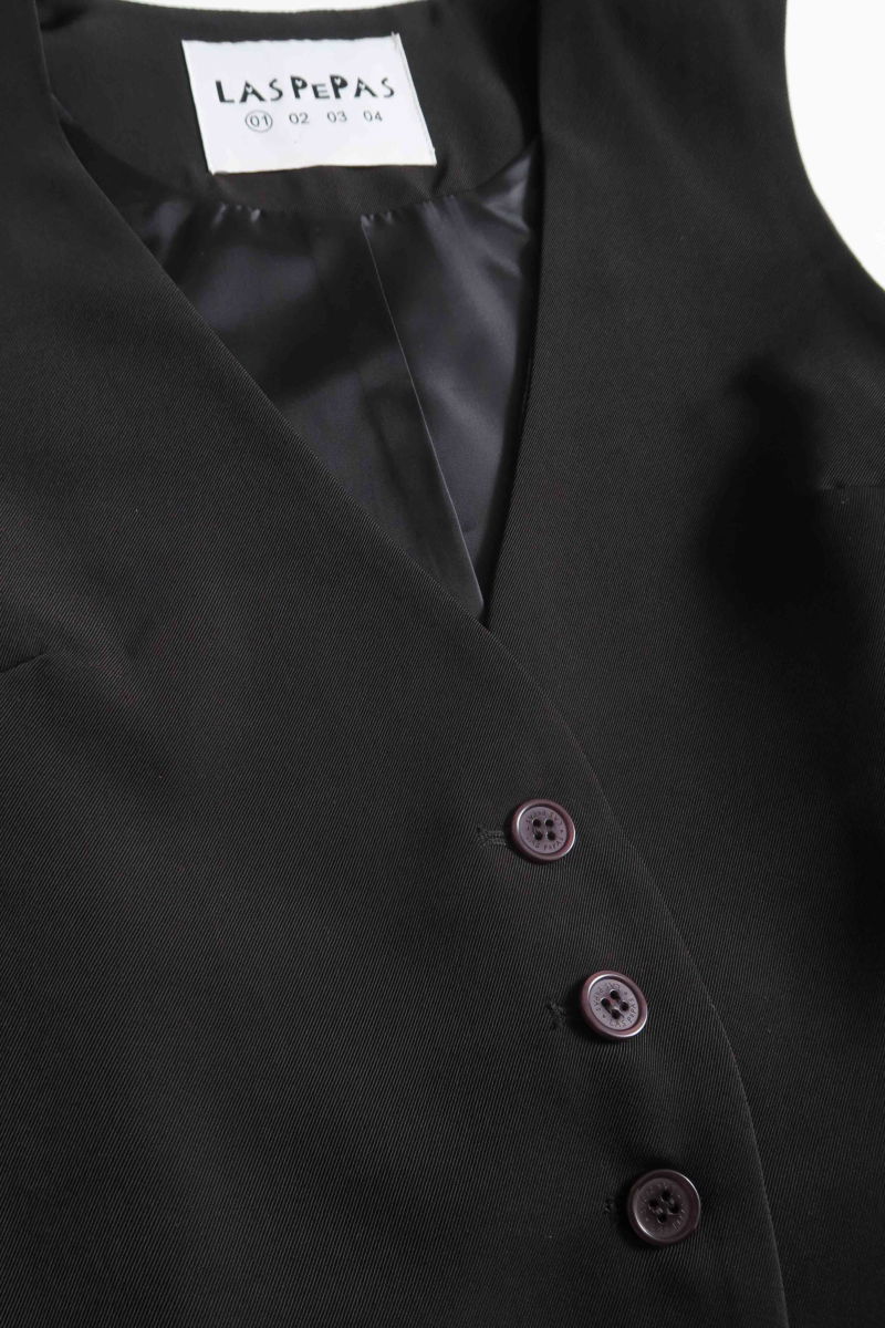 Chaleco sastrero negro con escote en V y largo a la cadera con botones a tono y lazo en la espalda. 