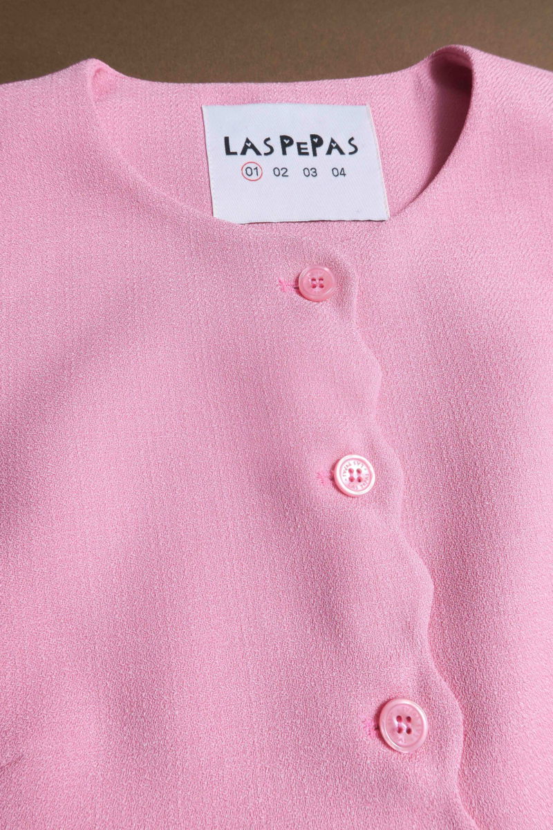 Chaleco rosa sastrero con terminación ondulada y botones a tono. 
