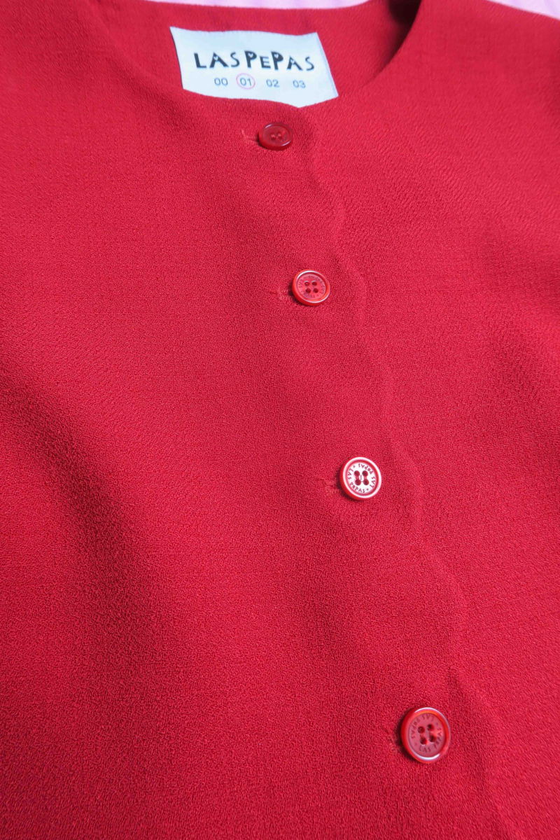 Chaleco rojo sastrero con terminación ondulada y botones a tono. 
