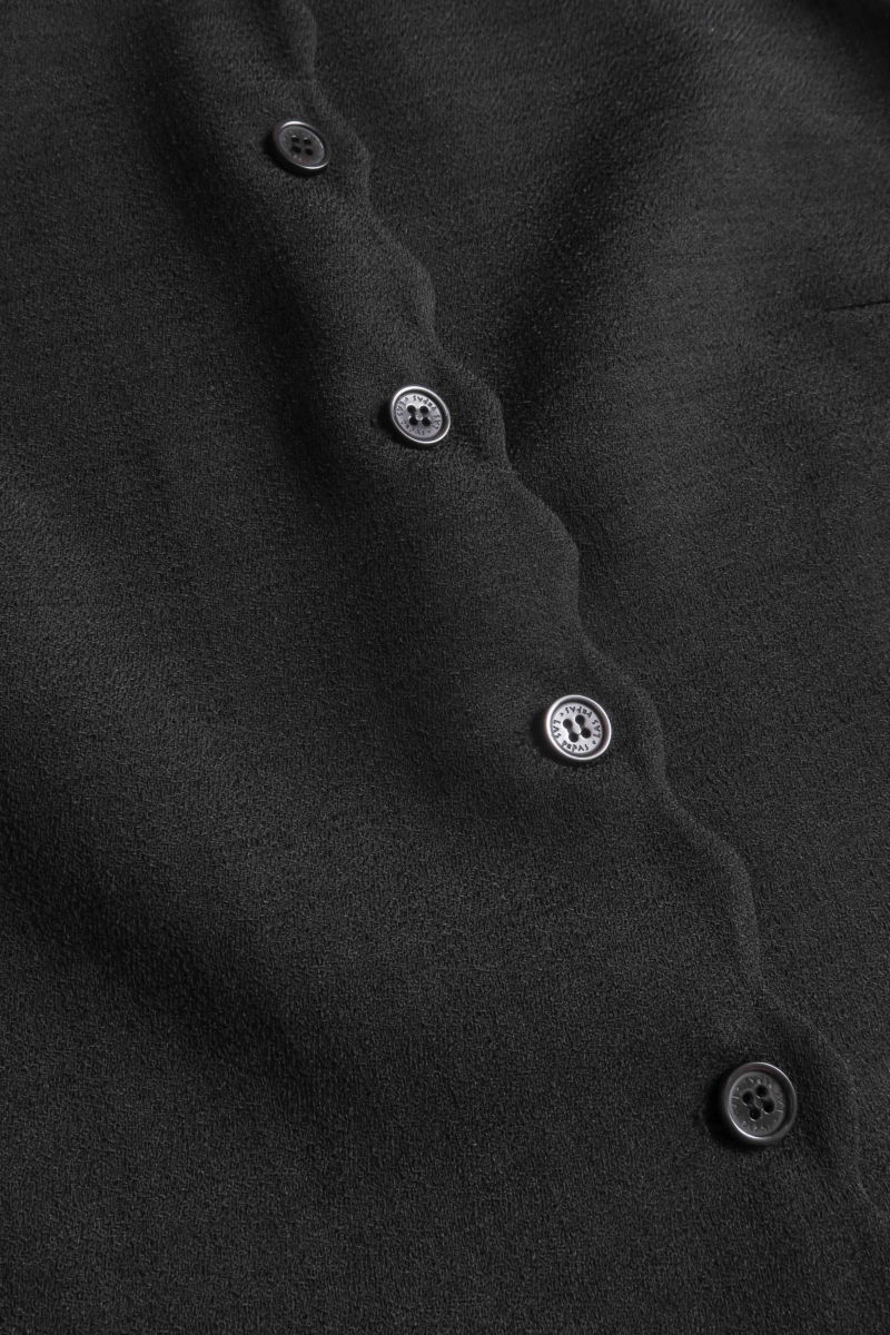 Chaleco negro sastrero con terminación ondulada y botones a tono. 
