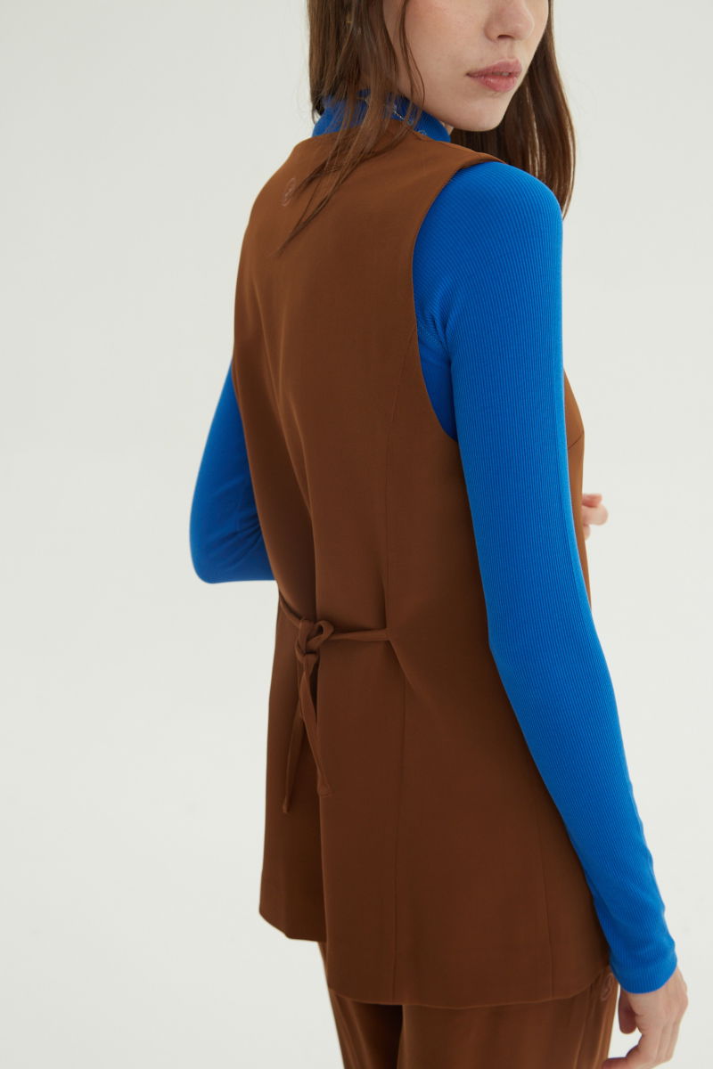 Chaleco sastrero suela con escote en V y largo a la cadera con botones a tono y lazo en la espalda. 