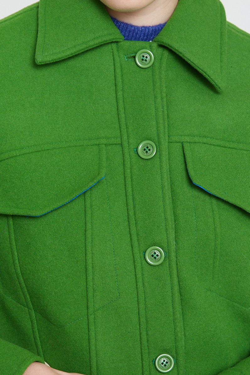 Campera verde de lana recta y larga hasta la cadera con sisas caídas, cuello en punta, botones a tono y bolsillos delanteros con solapa. 