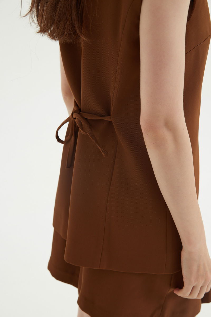 Chaleco sastrero suela con escote en V y largo a la cadera con botones a tono y lazo en la espalda. 