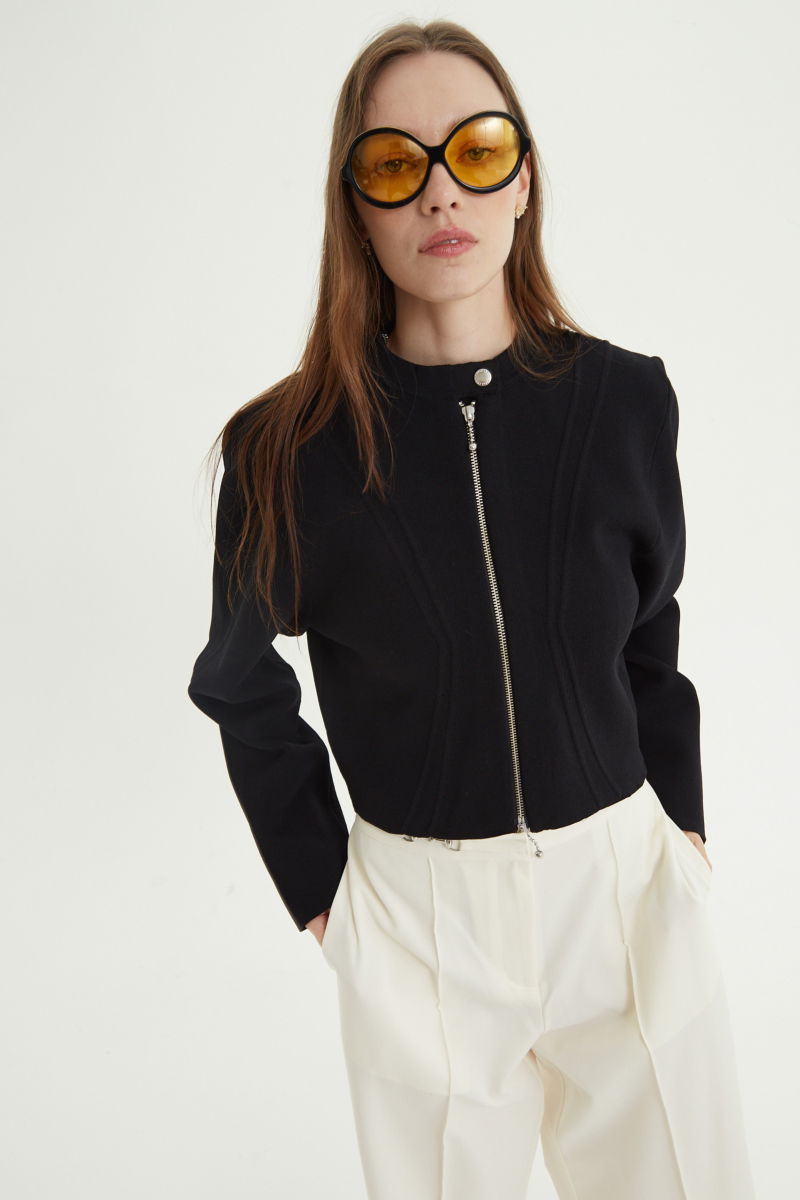 Campera negra tejida estilo bomber larga a la cadera con cierre doble camino, cuello mao con broche snap, hombros anchos y terminación redondeada en el ruedo.