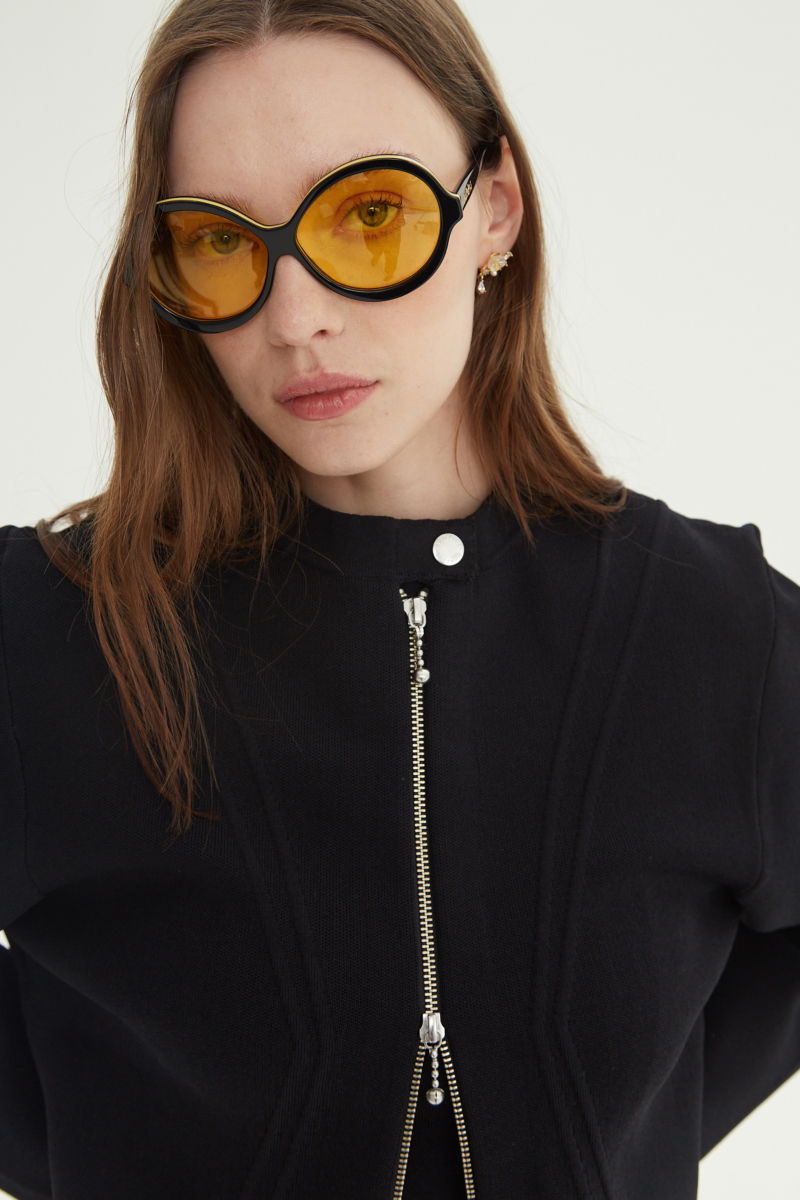 Campera negra tejida estilo bomber larga a la cadera con cierre doble camino, cuello mao con broche snap, hombros anchos y terminación redondeada en el ruedo.