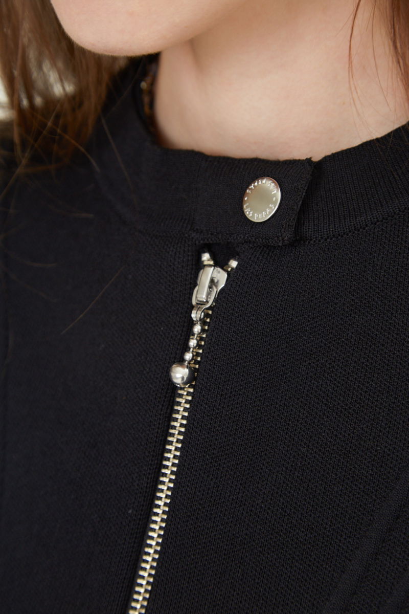 Campera negra tejida estilo bomber larga a la cadera con cierre doble camino, cuello mao con broche snap, hombros anchos y terminación redondeada en el ruedo.