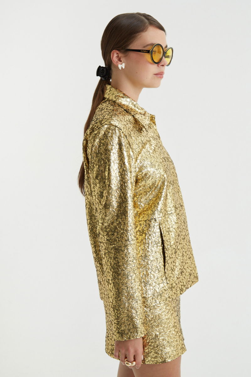 Campera de cuero metalizado con textura, de corte recto y larga debajo de la cadera con cierre escondido, cuello en punta y bolsillos laterales. 