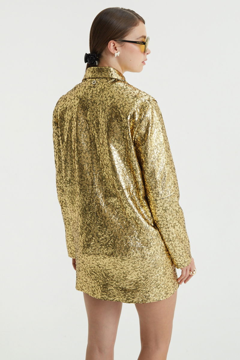 Campera de cuero metalizado con textura, de corte recto y larga debajo de la cadera con cierre escondido, cuello en punta y bolsillos laterales. 