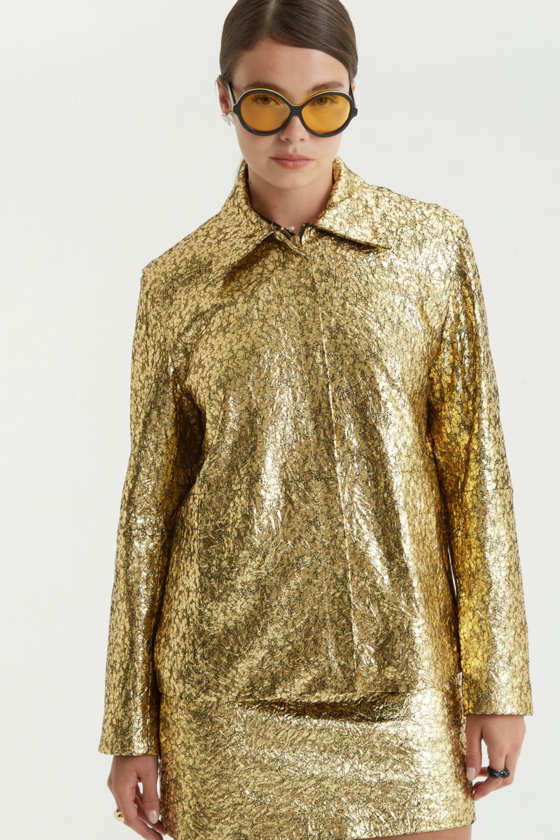 Campera de cuero metalizado con textura, de corte recto y larga debajo de la cadera con cierre escondido, cuello en punta y bolsillos laterales. 