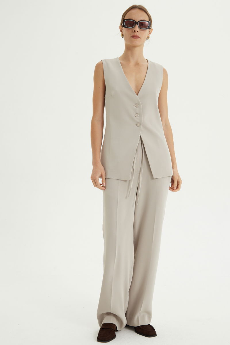 Pantalón beige sastrero tiro alto recto y largo a los tobillos con cintura con elástico y lazo a tono para atar. 