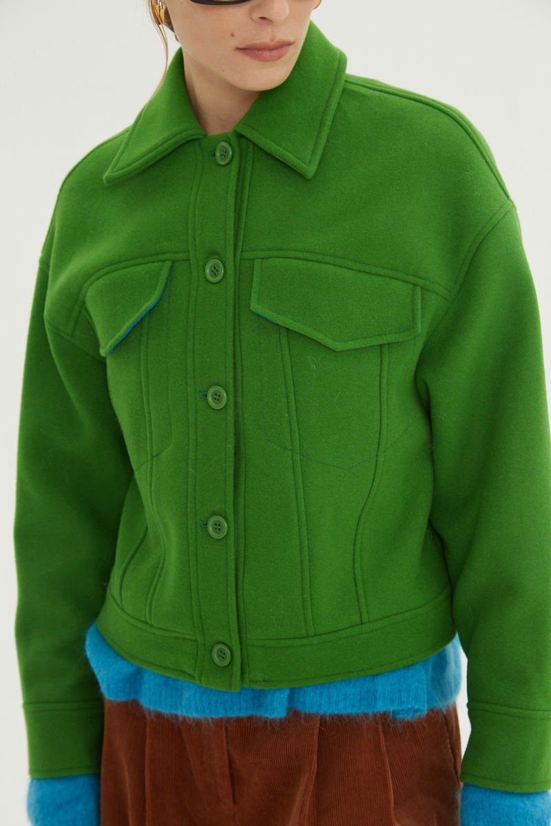 Campera verde de lana recta y larga hasta la cadera con sisas caídas, cuello en punta, botones a tono y bolsillos delanteros con solapa. 