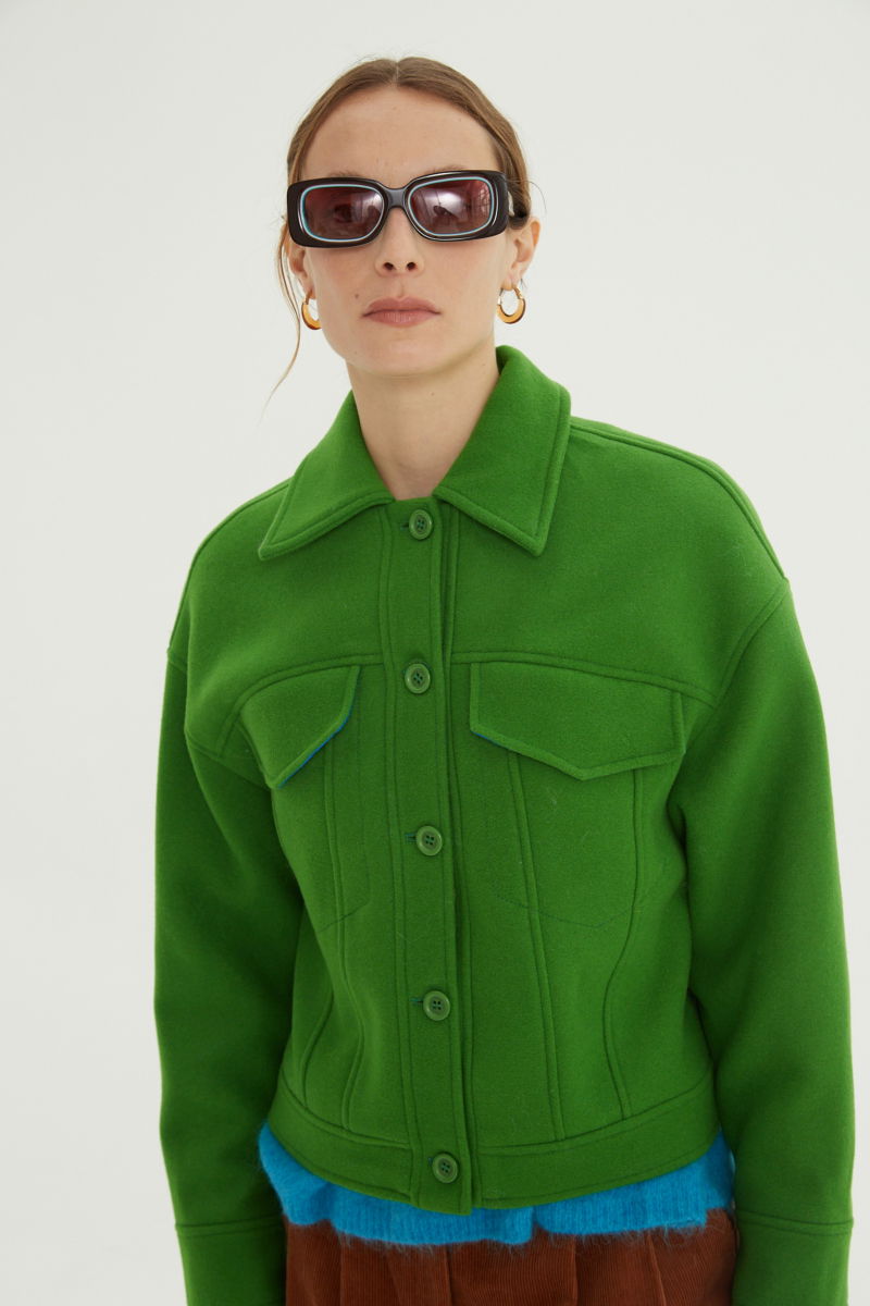 Campera verde de lana recta y larga hasta la cadera con sisas caídas, cuello en punta, botones a tono y bolsillos delanteros con solapa. 