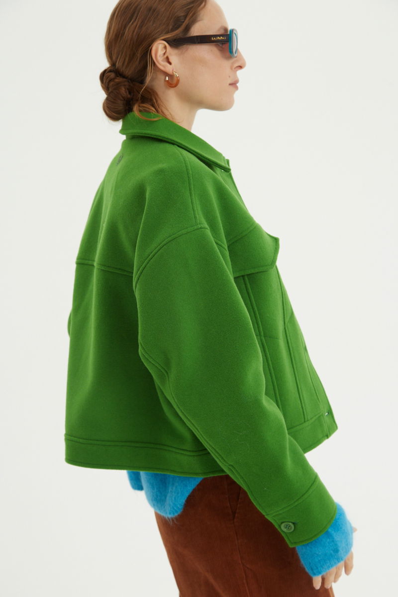 Campera verde de lana recta y larga hasta la cadera con sisas caídas, cuello en punta, botones a tono y bolsillos delanteros con solapa. 