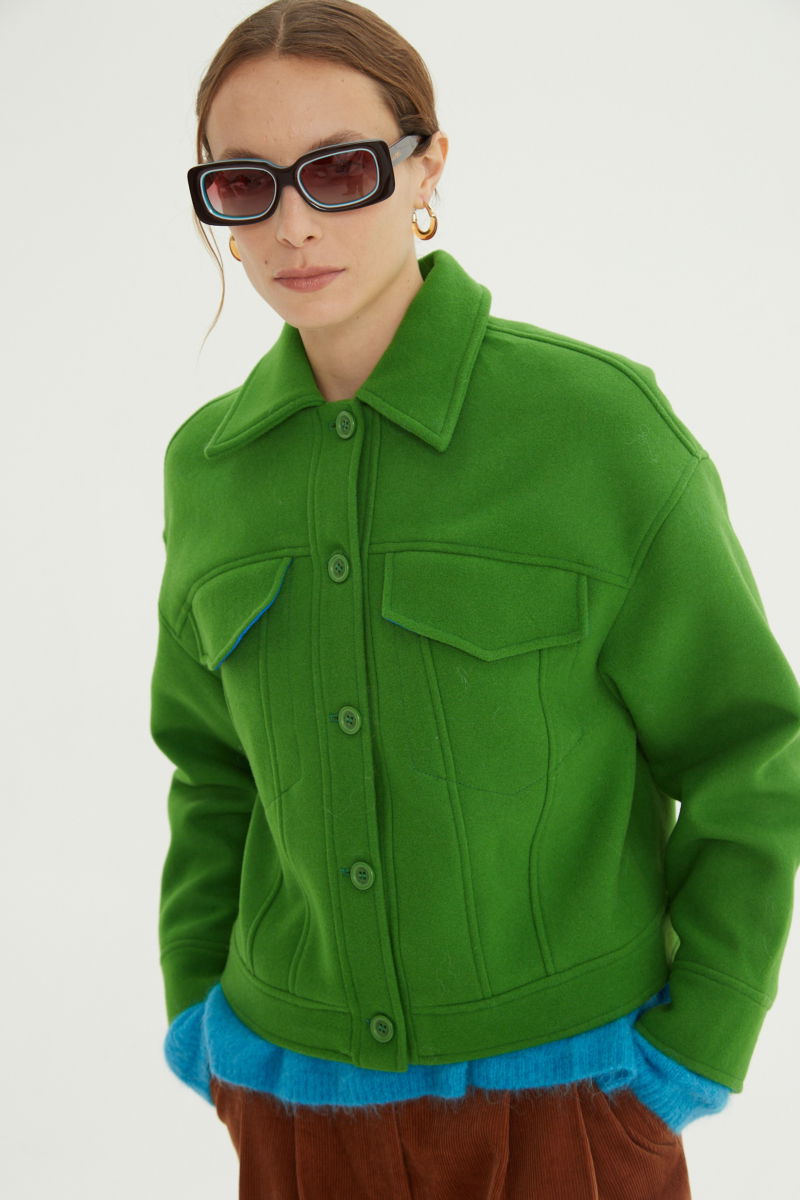 Campera verde de lana recta y larga hasta la cadera con sisas caídas, cuello en punta, botones a tono y bolsillos delanteros con solapa. 