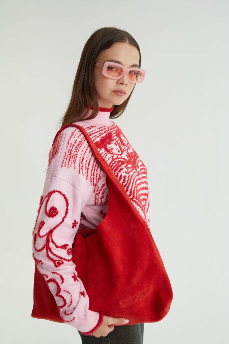 Maxi cartera roja de gamuza con broche con imán, logo de Las Pepas en el frente y bolso interno de red desmontable. 