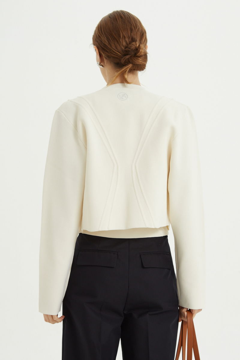 Campera crudo tejida estilo bomber larga a la cadera con cierre doble camino, cuello mao con broche snap, hombros anchos y terminación redondeada en el ruedo.