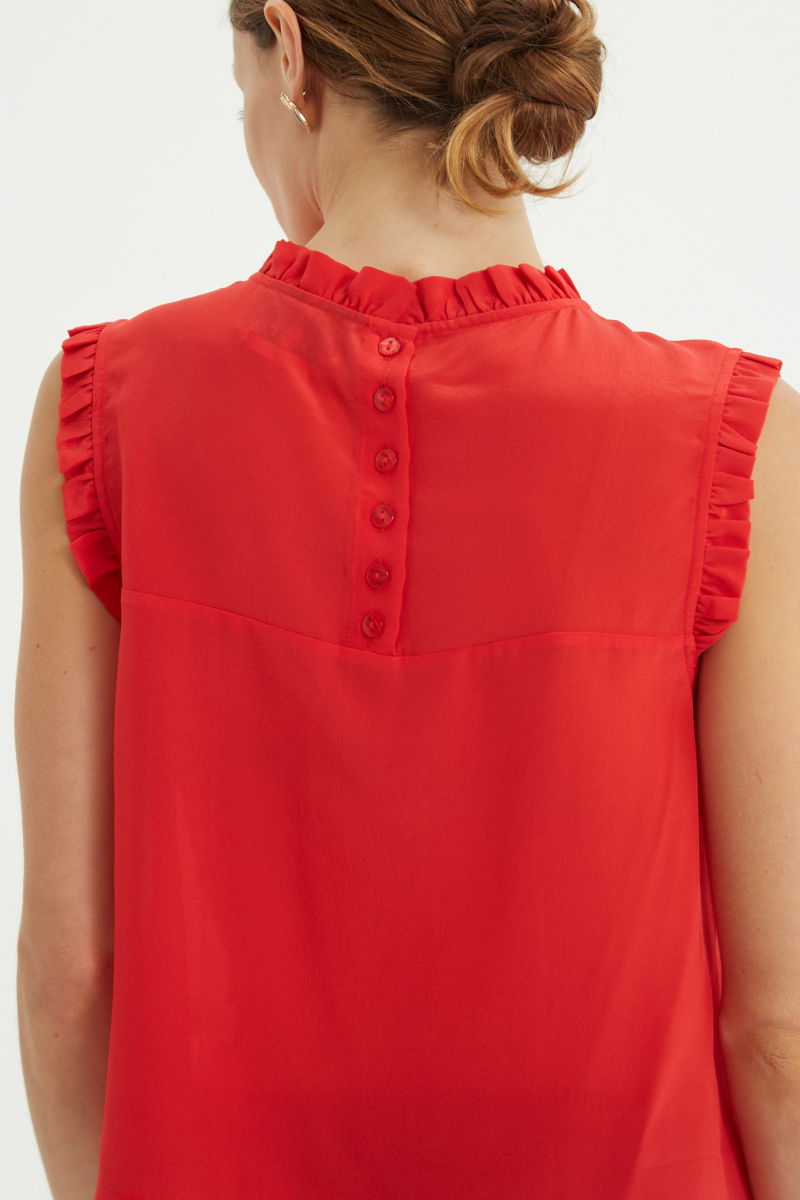 Musculosa roja de seda con volados en cuello y sisas, de corte recto y larga a la cadera con cuello mao y botones en la espalda. 
