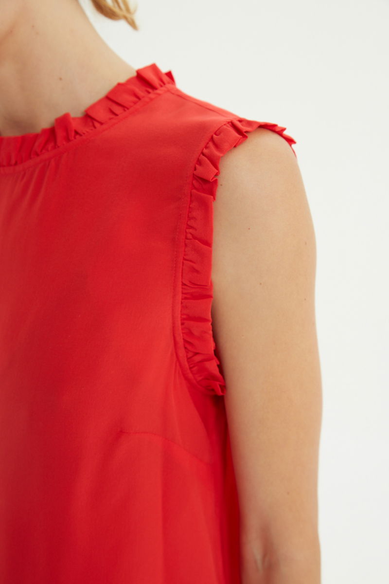 Musculosa roja de seda con volados en cuello y sisas, de corte recto y larga a la cadera con cuello mao y botones en la espalda. 
