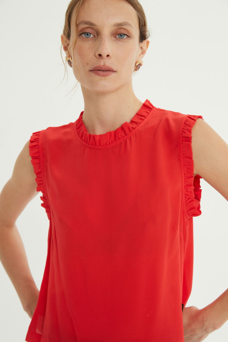 Musculosa roja de seda con volados en cuello y sisas, de corte recto y larga a la cadera con cuello mao y botones en la espalda. 
