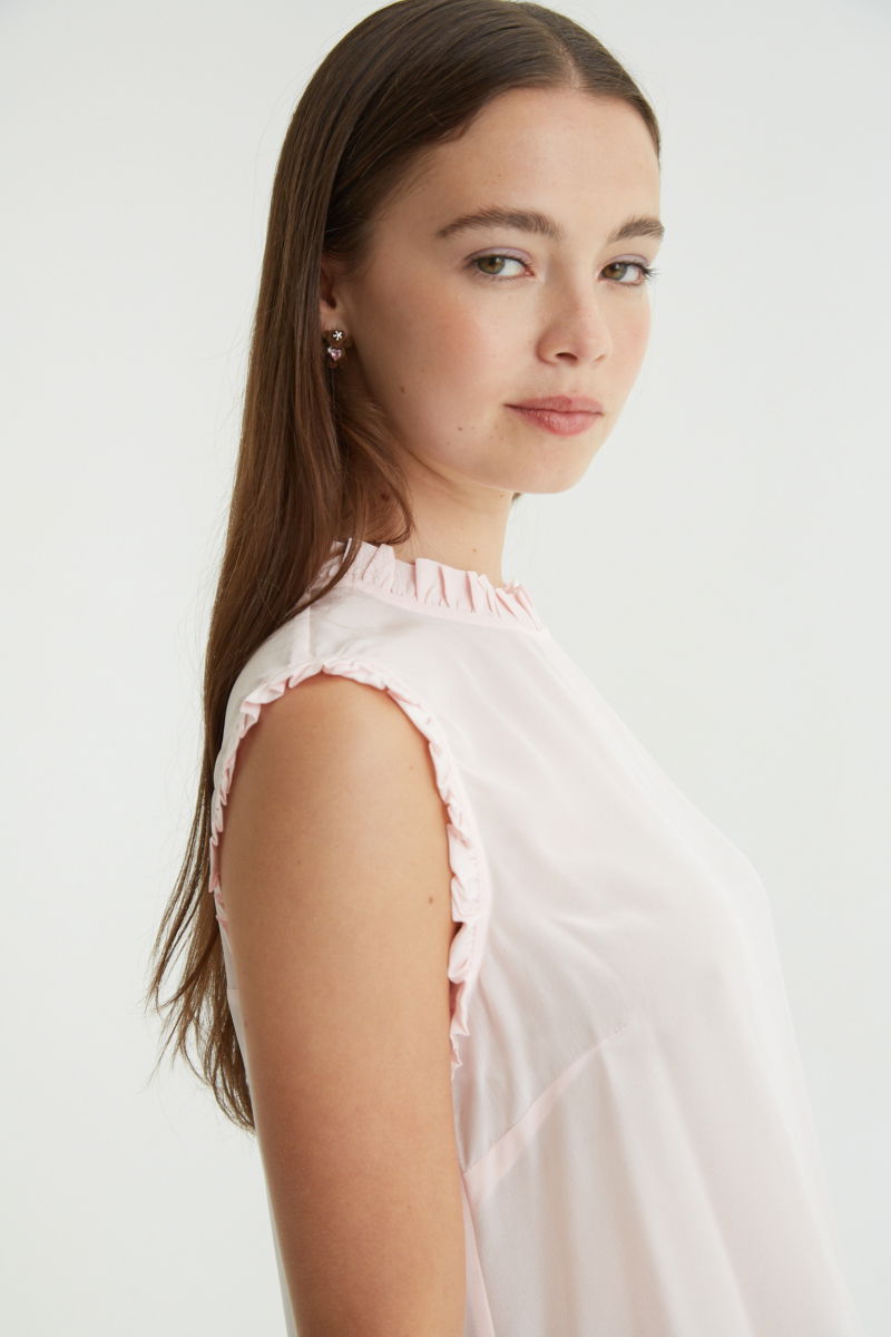 Musculosa rosa de seda con volados en cuello y sisas, de corte recto y larga a la cadera con cuello mao y botones en la espalda. 
