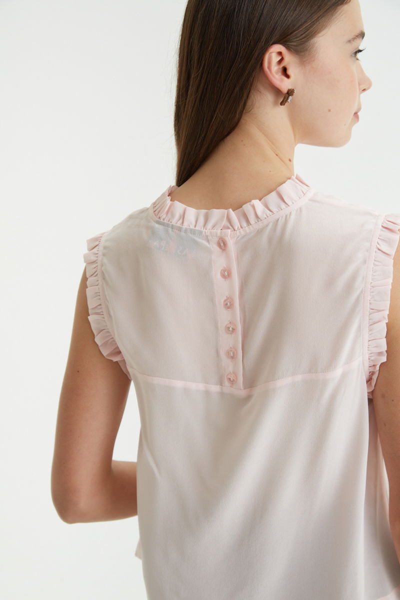 Musculosa rosa de seda con volados en cuello y sisas, de corte recto y larga a la cadera con cuello mao y botones en la espalda. 
