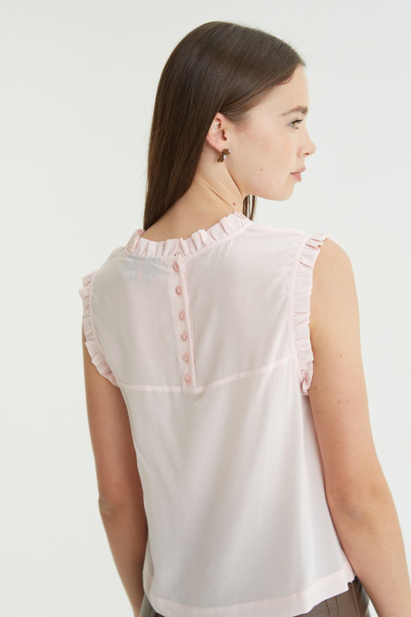 Musculosa rosa de seda con volados en cuello y sisas, de corte recto y larga a la cadera con cuello mao y botones en la espalda. 
