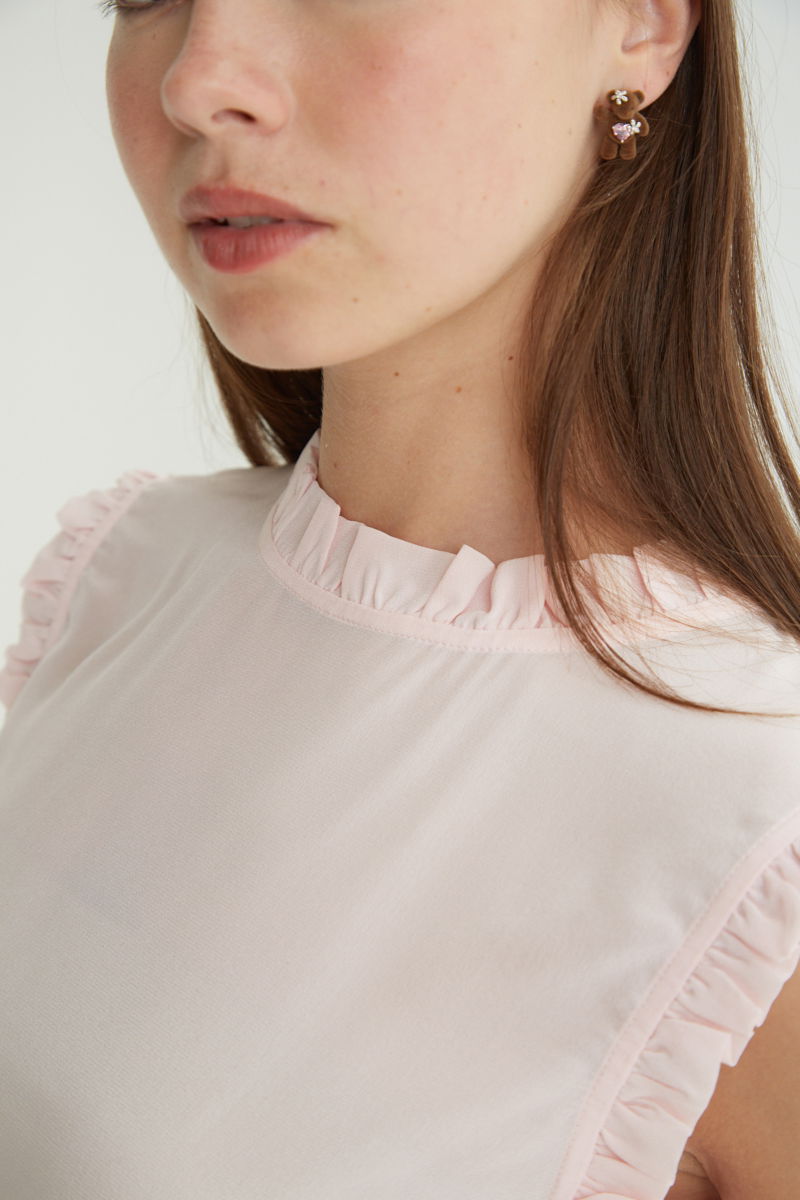 Musculosa rosa de seda con volados en cuello y sisas, de corte recto y larga a la cadera con cuello mao y botones en la espalda. 
