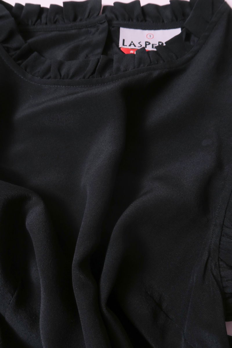 Musculosa negra de seda con volados en cuello y sisas, de corte recto y larga a la cadera con cuello mao y botones en la espalda. 
