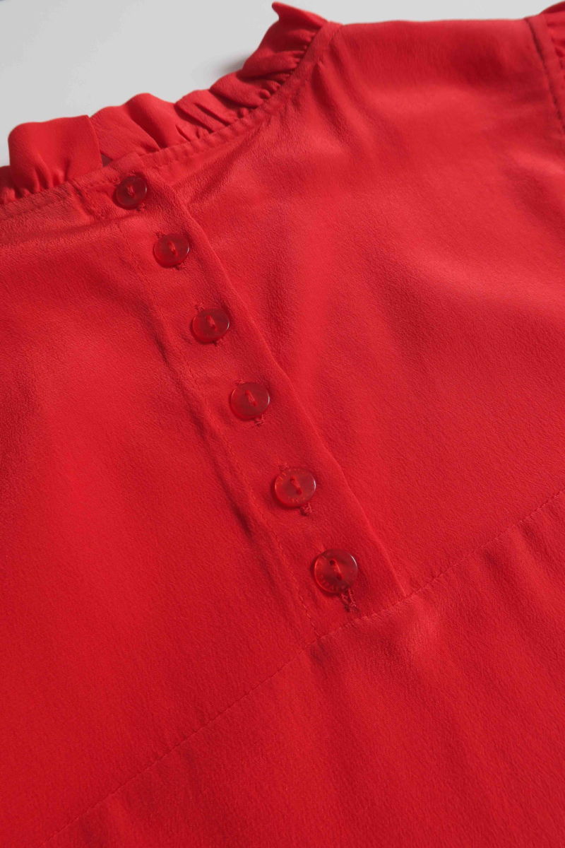 Musculosa roja de seda con volados en cuello y sisas, de corte recto y larga a la cadera con cuello mao y botones en la espalda. 
