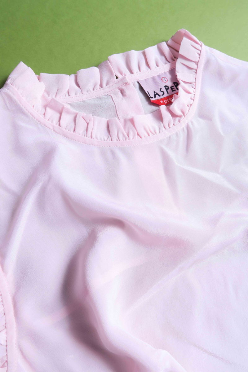 Musculosa rosa de seda con volados en cuello y sisas, de corte recto y larga a la cadera con cuello mao y botones en la espalda. 
