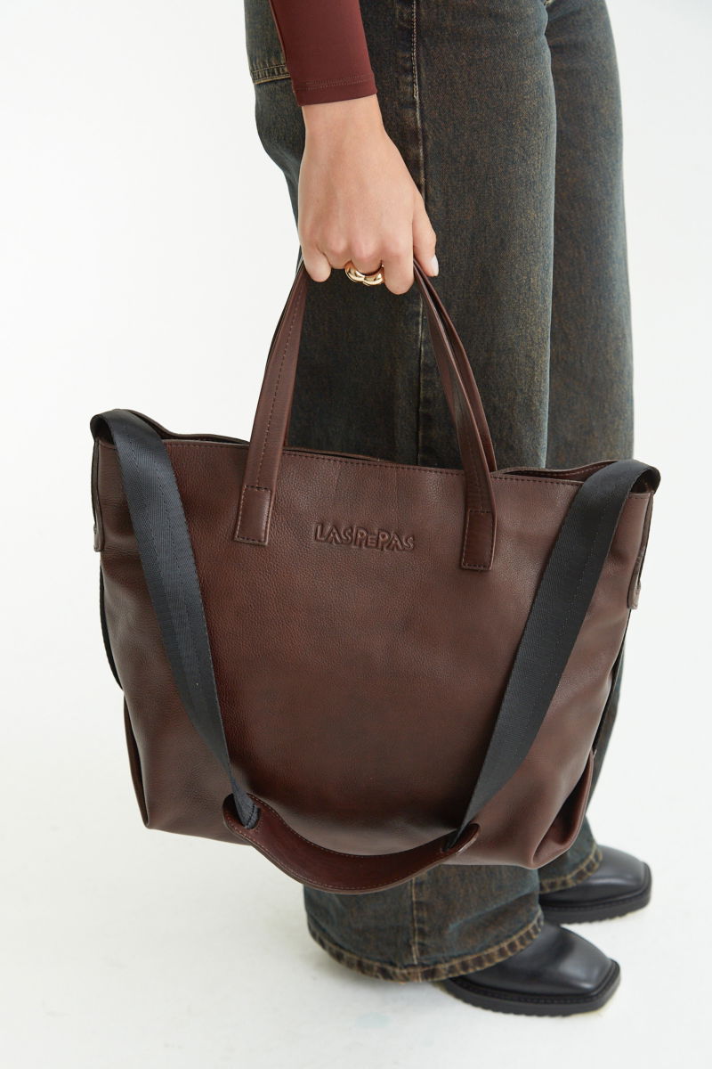 Cartera de cuero estilo shopper con logo grabado al frente, manijas cortas de cuero y correa larga de cinta mochilera.