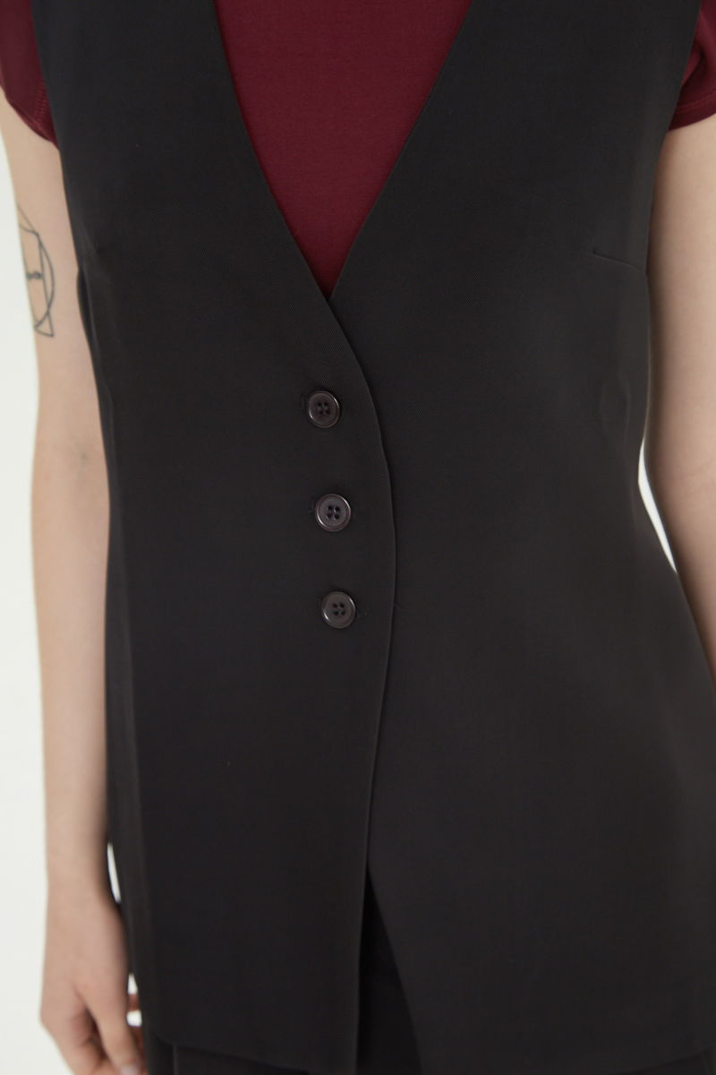 Chaleco sastrero negro con escote en V y largo a la cadera con botones a tono y lazo en la espalda. 