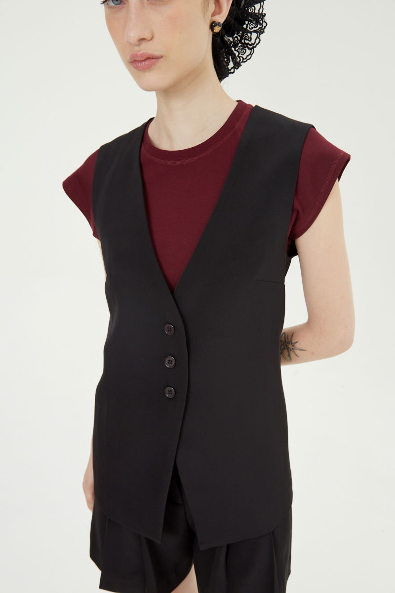 Chaleco sastrero negro con escote en V y largo a la cadera con botones a tono y lazo en la espalda. 