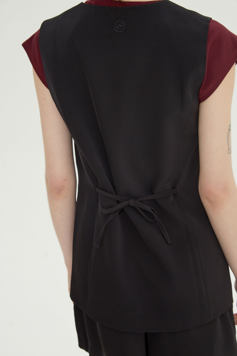 Chaleco sastrero negro con escote en V y largo a la cadera con botones a tono y lazo en la espalda. 