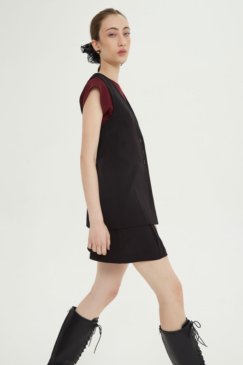 Chaleco sastrero negro con escote en V y largo a la cadera con botones a tono y lazo en la espalda. 