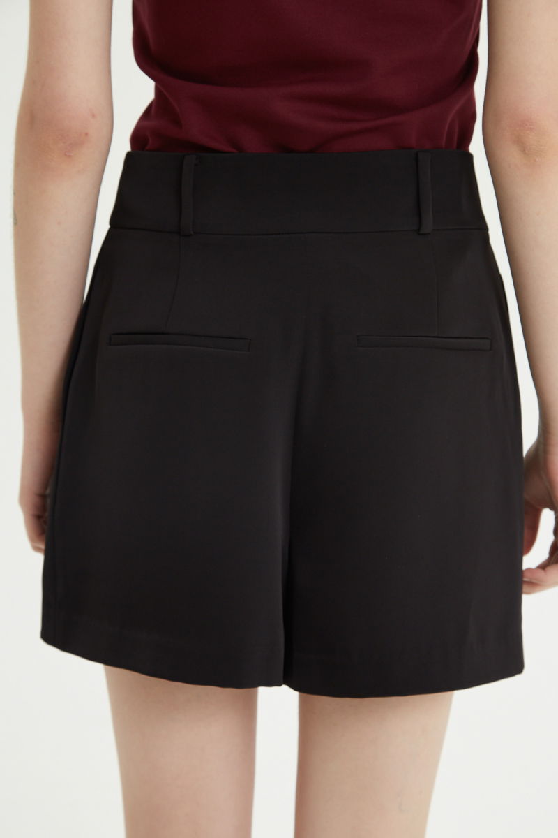 Short negro sastrero con pinzas delanteras, cintura ancha con presillas para cinturón y botones a tono, bolsillos laterales y bolsillos ojal traseros.
