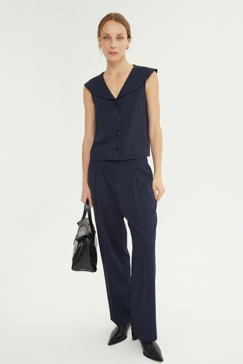 Pantalón azul sastrero tiro alto, de corte recto y largo hasta los tobillos con pinzas de entalle en frente y espalda. 