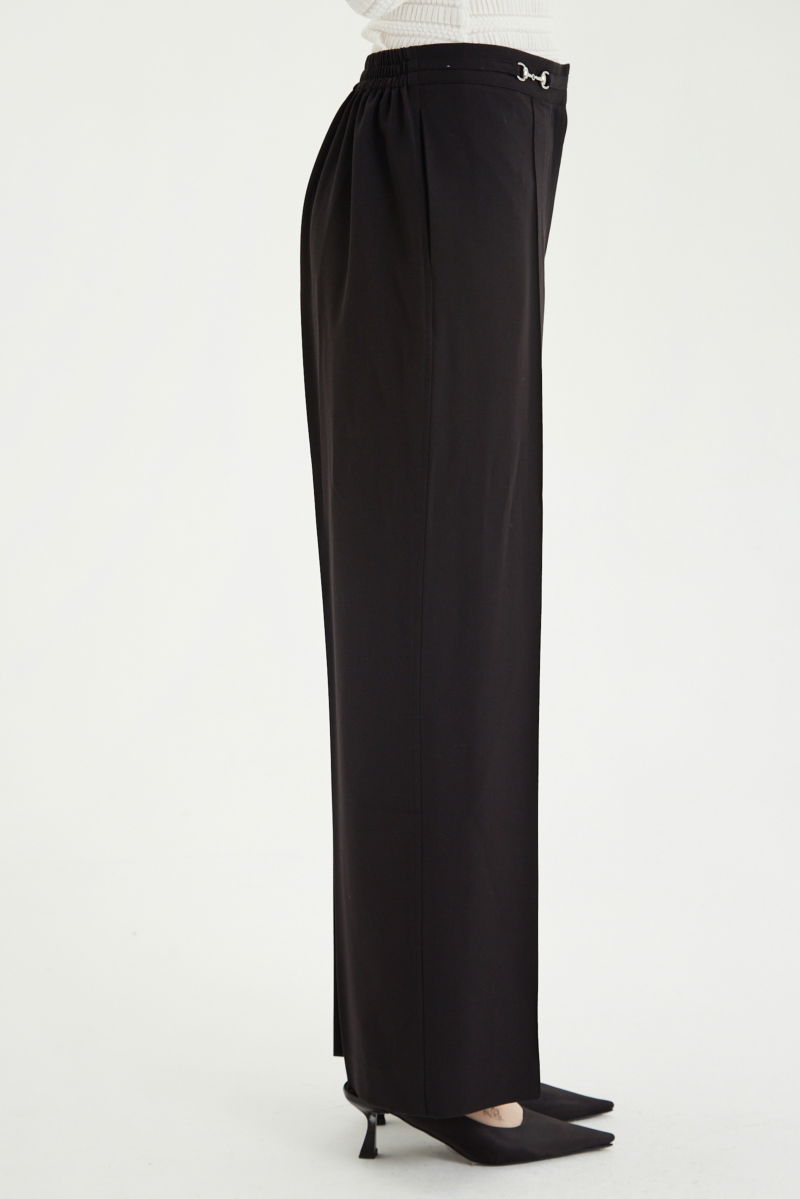 Pantalón negro sastrero tiro alto y recto con herrajes metálicos, pliegue en las piernas y elástico en la cintura trasera. 
