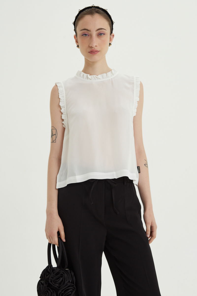 Musculosa cruda de seda con volados en cuello y sisas, de corte recto y larga a la cadera con cuello mao y botones en la espalda. 
