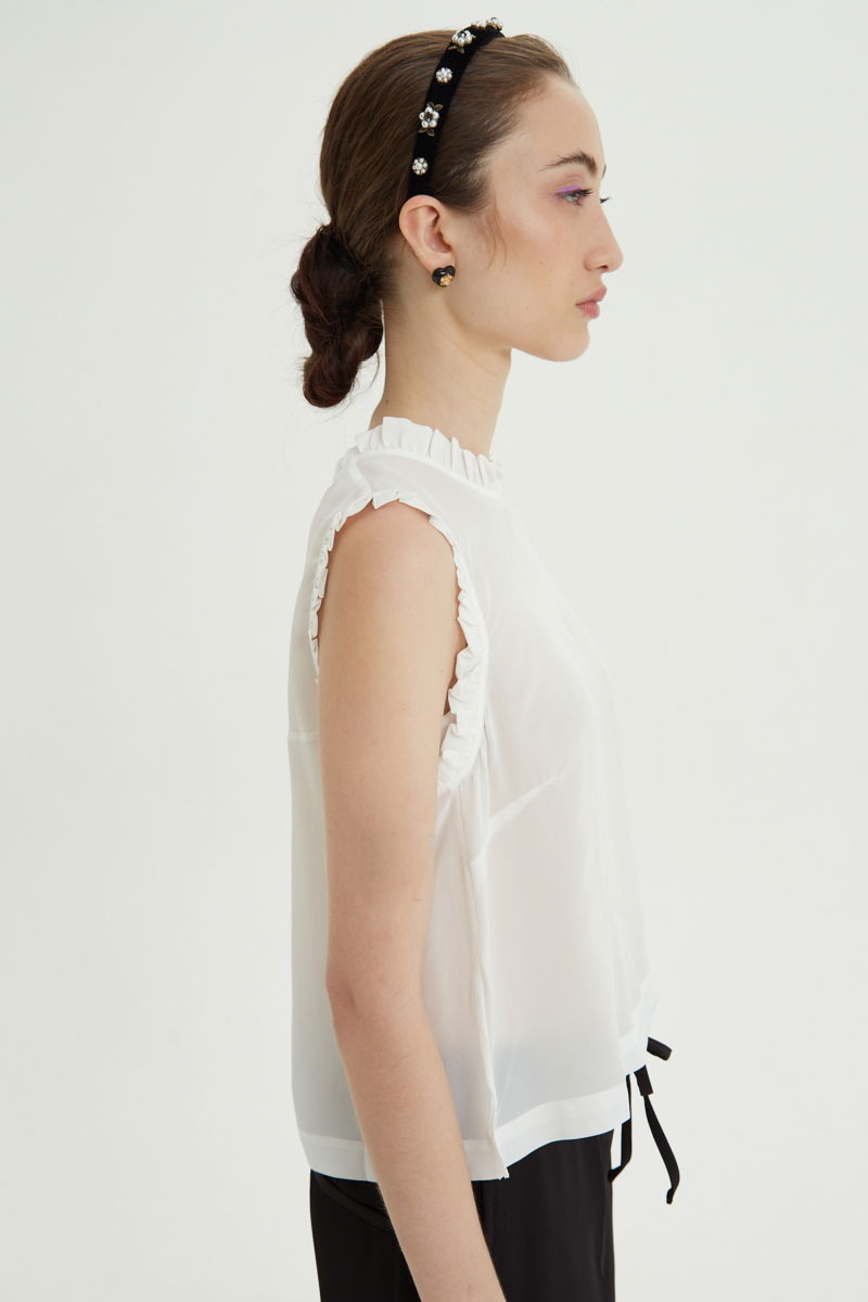 Musculosa cruda de seda con volados en cuello y sisas, de corte recto y larga a la cadera con cuello mao y botones en la espalda. 
