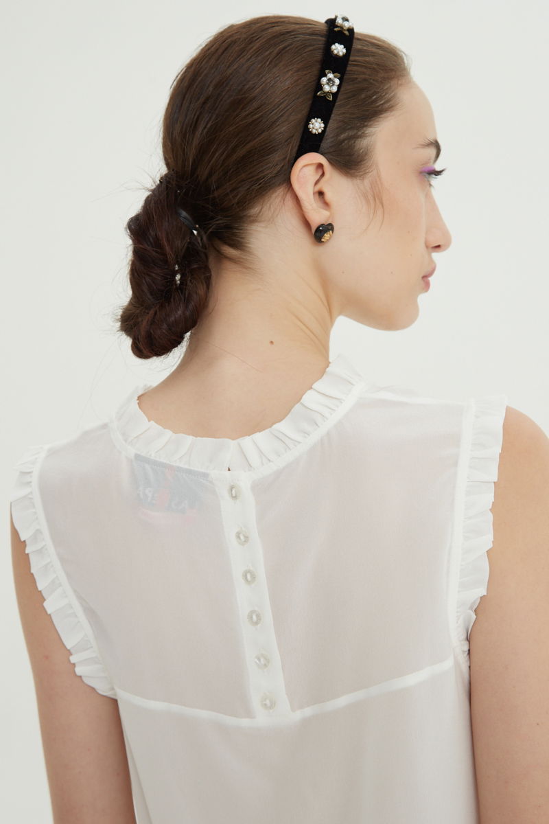 Musculosa cruda de seda con volados en cuello y sisas, de corte recto y larga a la cadera con cuello mao y botones en la espalda. 
