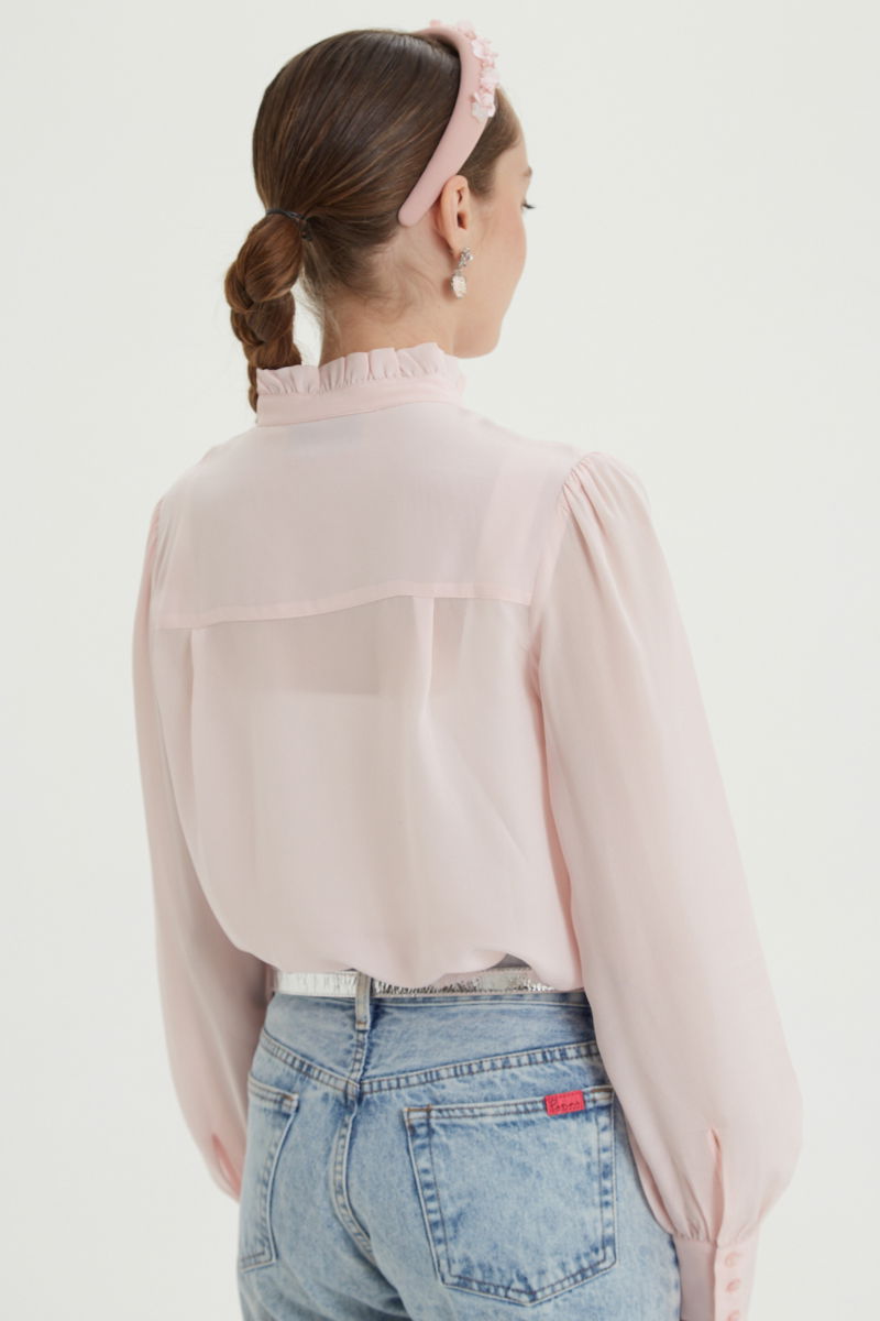 Camisa rosa de seda recta y larga a la cadera con cuello mao y volados en el cuello y la cartera, con frunces en los hombros y puños y botones a tono. 