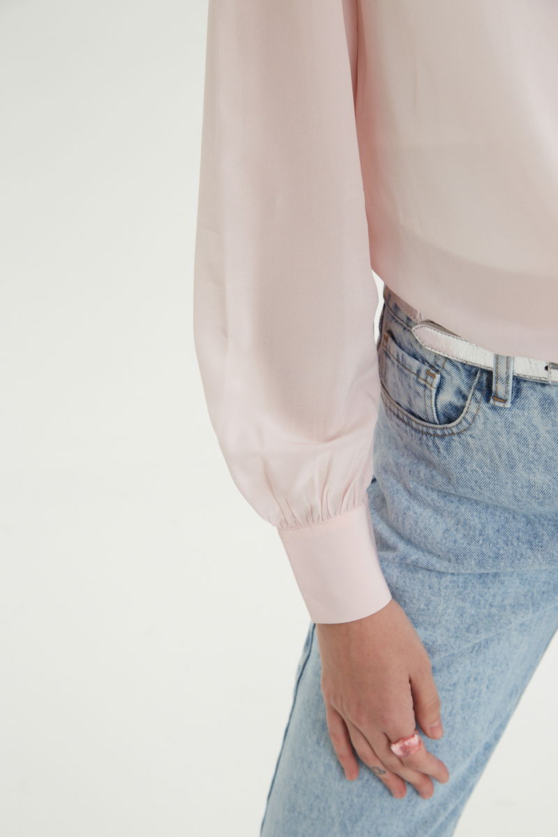 Camisa rosa de seda recta y larga a la cadera con cuello mao y volados en el cuello y la cartera, con frunces en los hombros y puños y botones a tono. 