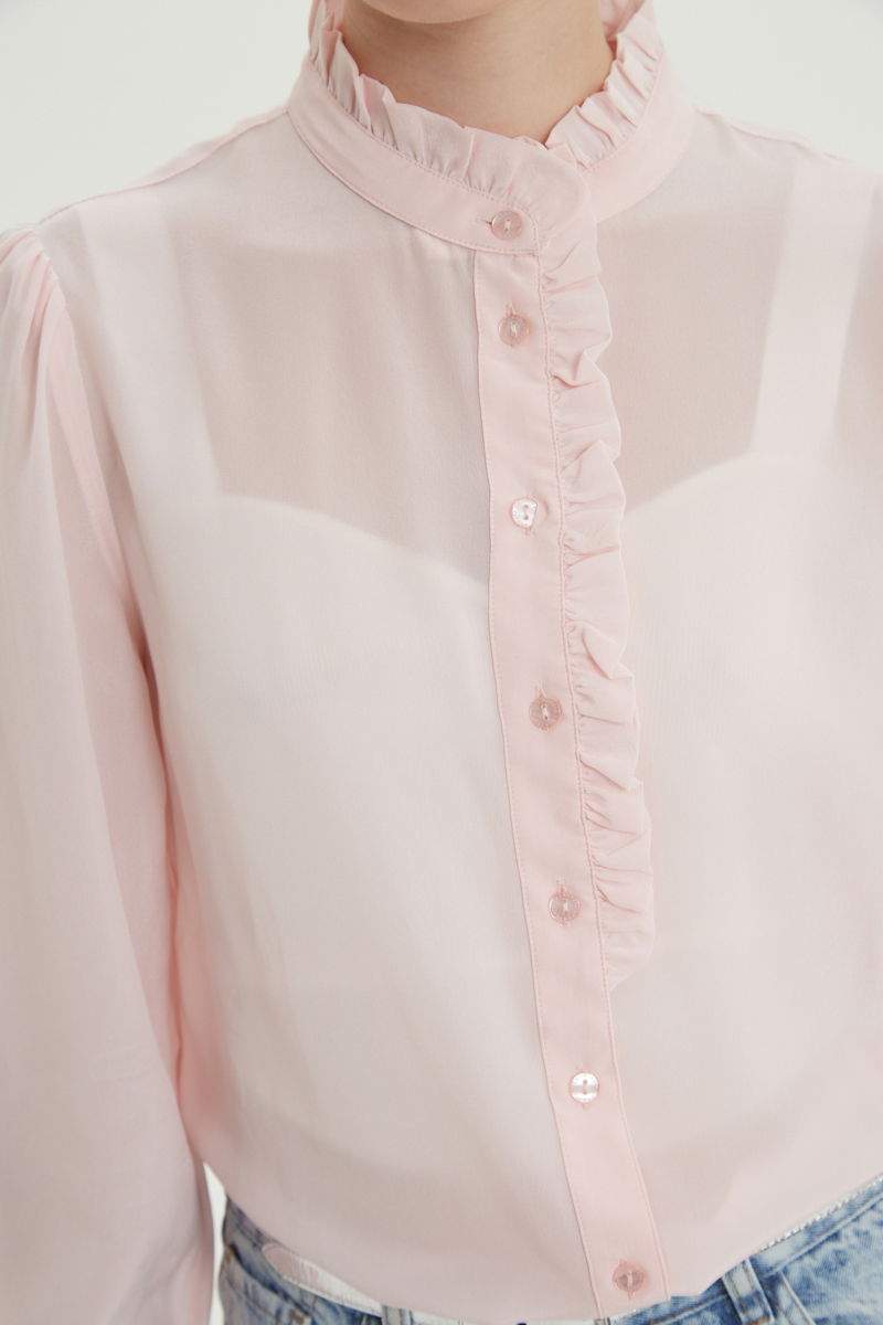 Camisa rosa de seda recta y larga a la cadera con cuello mao y volados en el cuello y la cartera, con frunces en los hombros y puños y botones a tono. 