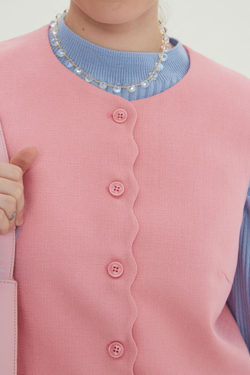 Chaleco rosa sastrero con terminación ondulada y botones a tono. 
