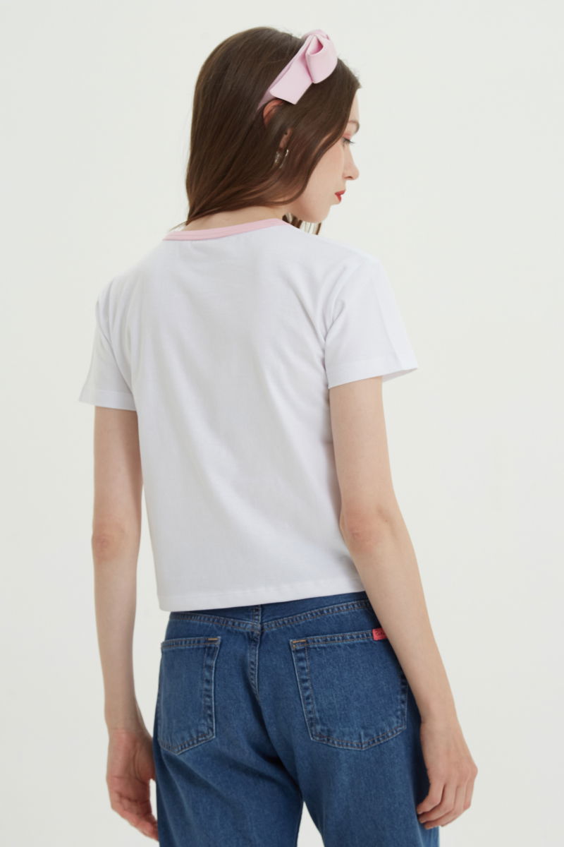 Remera de algodón con estampa central, manga corta, recta y larga hasta la cadera con cuello redondo con terminación de ribb rosa y moño de cinta de raso.